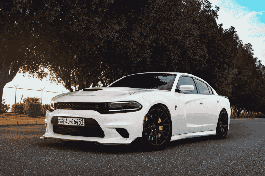 White Dodge Charger Hellcat parked on a black asphalt road, with surrounding trees bathed in the light of sunset.