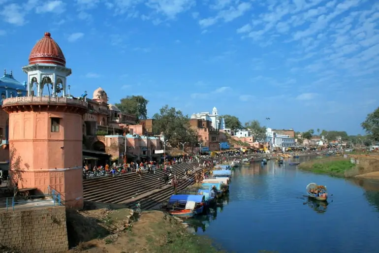 Chitrakoot Dham: A Journey Through Lord Rama's Sacred Abode A scenic view of Chitrakoot Dham, showcasing ancient temples, bustling river ghats, and boats on the calm waters under a bright blue sky, reflecting its spiritual charm.